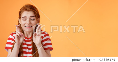 Close-up dreamy cute tender ginger girl make wish, cross fingers good luck closed eyes bite lip eager win lottery, supplicating, praying dream come true, stand orange background believe miracle 98116375