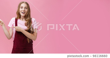 Woman looking with impressed and amazed look showing cool think on left side of copy space smiling fascinated looking with admiration at camera standing delighted and surprised over pink background 98116660