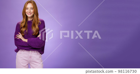 Portrait of pretty young and happy 20s ginger girl in purple sweater holding hands crossed over body smiling broadly, feeling self-assured as promoting project with confidence over violet wall Portrait of pretty young and happy 20s ginger girl in purple sweater holding hands crossed over body smiling broadly, feeling self-assured as promoting project with confidence over violet wall 98116730