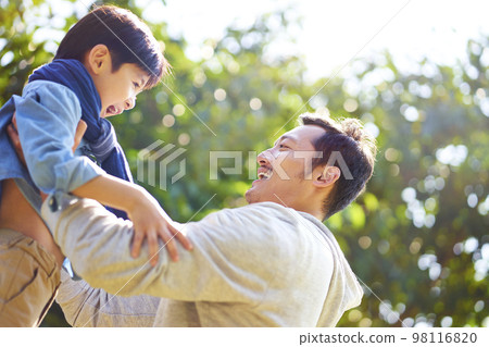 asian father having fun lifting son oudoors in park. 98116820