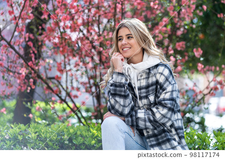 Pretty Caucasian young woman dressed in coat with some flowers in the background 98117174