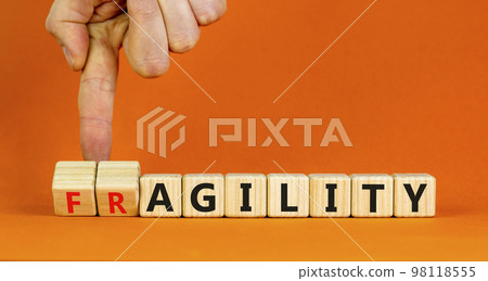 Fragility or agility symbol. Concept words Fragility and Agility on wooden cubes. Businessman hand. Beautiful orange table orange background. Business fragility and agility concept. Copy space. 98118555