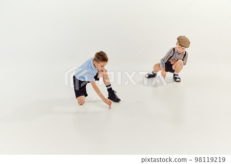 Two boys, children in classical retro clothes drawing on floor with chalks over grey studio background. Concept of game, childhood, friendship 98119219