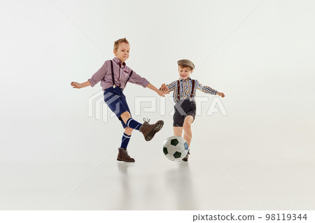 Competition. Boys, children in classical retro clothes playing football over grey studio background. Concept of game, childhood, friendship Competition. Boys, children in classical retro clothes playing football over grey studio background. Concept of game, childhood, friendship 98119344