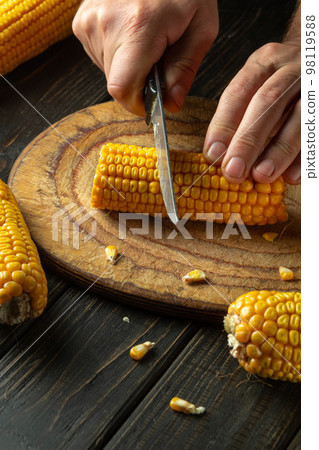 The cook cuts corn with a knife. Maize is a great diet breakfast or lunch. Working environment at the kitchen table. 98119588