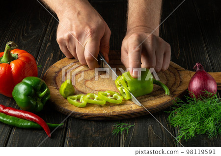 Close-up of the cook hands with a knife cut fresh pepper on the cutting board of the restaurant kitchen. Vegetarian diet 98119591