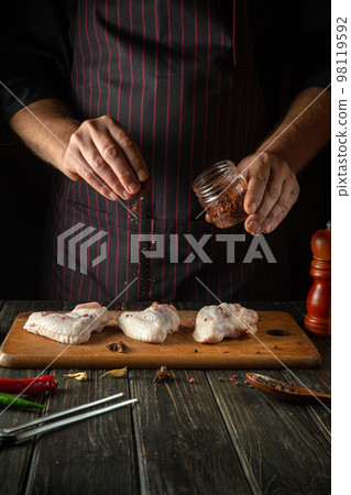 The chef adds aromatic spices to raw chicken wings. Cooking chicken nugget in the restaurant kitchen The chef adds aromatic spices to raw chicken wings. Cooking chicken nugget in the restaurant kitchen 98119592