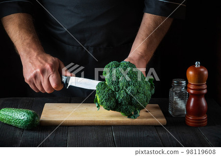 Cook cuts fresh Broccoli with a knife for salad on vintage kitchen table with fresh vegetables. Cooking and restaurant or cafe concept 98119608