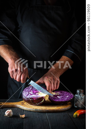 The cook is cutting red cabbage with a knife. Cooking vegetable salad in the restaurant kitchen. Vegetable diet idea. 98119609