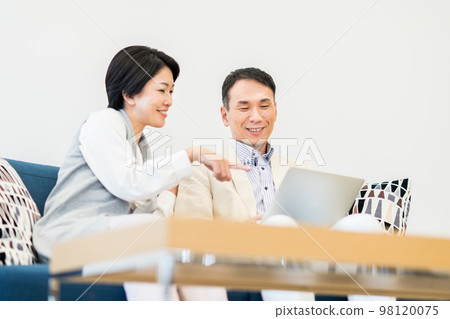 Middle-aged couple looking at a computer in the living room Middle-aged couple looking at a computer in the living room 98120075