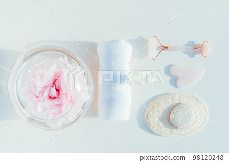 Cosmetic facial kit for home skin care and spa. Face roller, gua sha massage, essential oil serum, towel, pads and peony in vase on white background. Natural treatment concept. Top view. Flat lay Cosmetic facial kit for home skin care and spa. Face roller, gua sha massage, essential oil serum, towel, pads and peony in vase on white background. Natural treatment concept. Top view. Flat lay 98120248