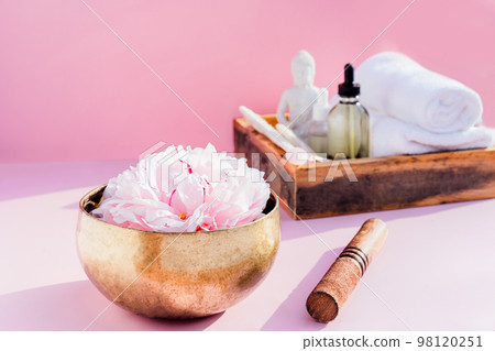 Tibetan singing bowl with floating peony flower and spa wellness exotic massage set on the pink background. Asian relaxing spa procedure with essential oils. Alternative medicine and body care. Tibetan singing bowl with floating peony flower and spa wellness exotic massage set on the pink background. Asian relaxing spa procedure with essential oils. Alternative medicine and body care. 98120251