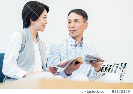 A middle-aged couple looking at a magazine in the living room A middle-aged couple looking at a magazine in the living room 98120399