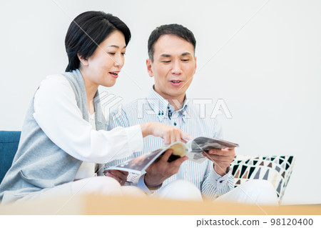 A middle-aged couple looking at a magazine in the living room A middle-aged couple looking at a magazine in the living room 98120400