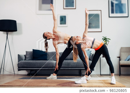 Woman and girl working out at home, doing side bends. 98120805