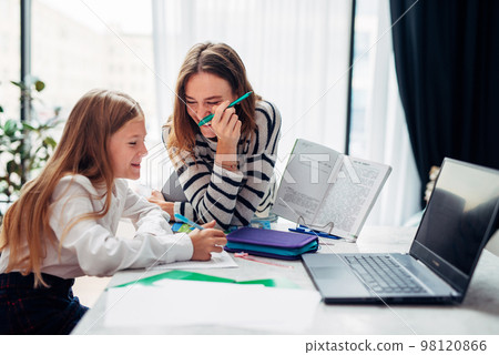 Mother and daughter laughing while doing homework Mother and daughter laughing while doing homework 98120866