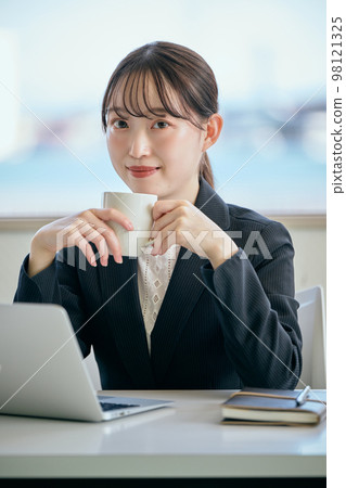Young woman taking a break with coffee at her desk Young woman taking a break with coffee at her desk 98121325
