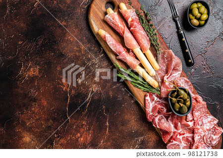 Meat appetizer platter with grissini sticks, Prosciutto crudo, Salami and Coppa Sausage and olives. Dark background. Top view. Copy space Meat appetizer platter with grissini sticks, Prosciutto crudo, Salami and Coppa Sausage and olives. Dark background. Top view. Copy space 98121738