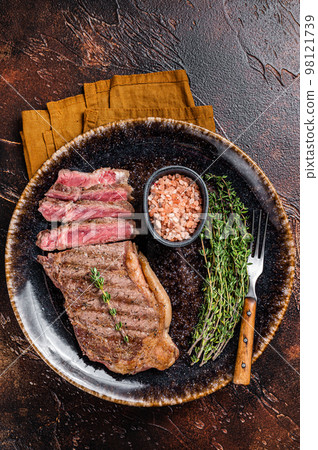 BBQ roast sliced New York beef steak on a plate with thyme and salt. Dark background. Top view 98121739