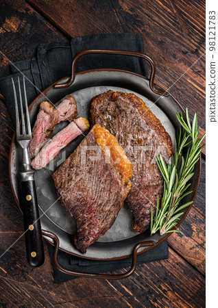 Grilled picanha or top sirloin beef steak with rosemary in steel tray. Wooden background. Top view 98121783