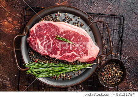Raw New York or striploin beef meat steak with rosemary and pepper. Dark background. Top view 98121784