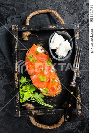 Sandwich with salmon fillet and cream cheese in wooden tray. Black background. Top view 98121785