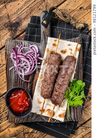 Traditional middle east kefta, kofta kebab from ground beef and lamb meat grilled on skewers served with flatbread and onion. Wooden background. Top view Traditional middle east kefta, kofta kebab from ground beef and lamb meat grilled on skewers served with flatbread and onion. Wooden background. Top view 98121799