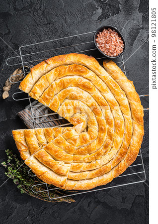 Turkish Tepsi Boregi, Round Borek cheese pie on kitchen board. Black background. Top view Turkish Tepsi Boregi, Round Borek cheese pie on kitchen board. Black background. Top view 98121805