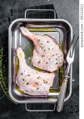 Raw meat, duck legs thighs with herbs and ingredients in a steel tray. Black background. Top view Raw meat, duck legs thighs with herbs and ingredients in a steel tray. Black background. Top view 98121821
