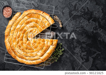 Turkish Tepsi Boregi, Round Borek cheese pie on kitchen board. Black background. Top view. Copy space 98121825