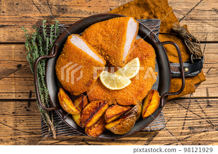 Delicious crispy pork schnitzel with fried potato wedges. Wooden background. Top view 98121929