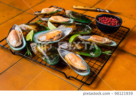 Raw green kiwi mussels in shells with herbs. Orange background. Top view Raw green kiwi mussels in shells with herbs. Orange background. Top view 98121939