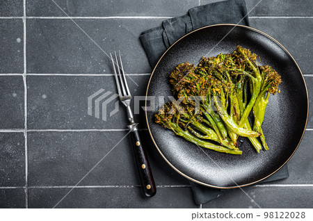Roasted green Broccolini Sprouts with garlic butter in a plate. Black background. Top view. Copy space 98122028