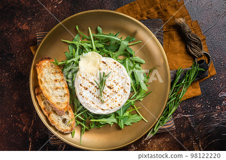 Salad with grilled Camembert cheese, arugula, toast and rosemary in a plate. Dark background. Top view Salad with grilled Camembert cheese, arugula, toast and rosemary in a plate. Dark background. Top view 98122220
