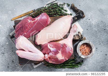 Butchered whole duck, raw breast steak, legs, wings on a butcher cutting board. Gray background. Top view Butchered whole duck, raw breast steak, legs, wings on a butcher cutting board. Gray background. Top view 98122295