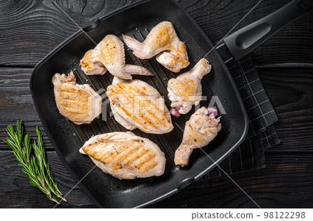 Roasted on a grill skillet chicken meat and chicken parts - drumstick, breast fillet, wing, thigh. Black wooden background. Top view 98122298