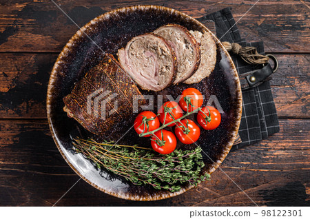 Sliced roast pork roulade - Porchetta on a plate with spices. Wooden background. Top view Sliced roast pork roulade - Porchetta on a plate with spices. Wooden background. Top view 98122301