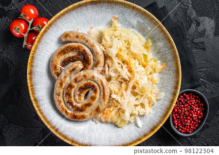Roast bavarian spiral meat sausages on a plate with sauerkraut. Black background. Top view 98122304