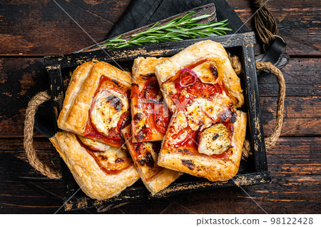 Puff pastry tart pizza with artichoke, mozzarella, tomatoes and cheese sliced in a wooden tray. Wooden background. Top view Puff pastry tart pizza with artichoke, mozzarella, tomatoes and cheese sliced in a wooden tray. Wooden background. Top view 98122428