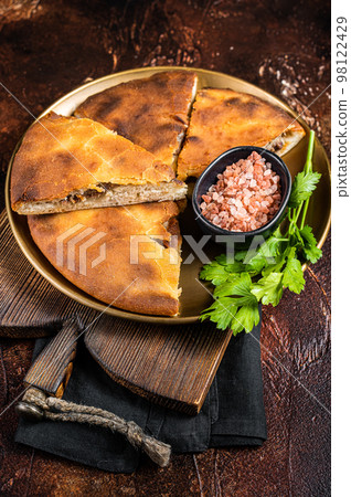 Traditional Ossetian pie sliced on a plate. Dark background. Top view Traditional Ossetian pie sliced on a plate. Dark background. Top view 98122429