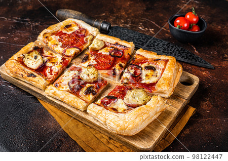 Vegetarian puff pastry pizza with artichoke, mozzarella, tomatoes and cheese sliced on a wooden board. Dark background. Top view Vegetarian puff pastry pizza with artichoke, mozzarella, tomatoes and cheese sliced on a wooden board. Dark background. Top view 98122447