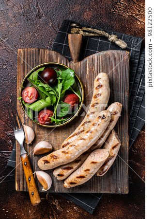 BBQ fried pork meat sausages served with greens on wooden board. Dark background. Top view BBQ fried pork meat sausages served with greens on wooden board. Dark background. Top view 98122500