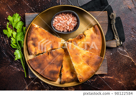 Traditional Ossetian pie sliced on a plate. Dark background. Top view 98122584