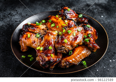 Baked chicken wings with sweet chili sauce in a plate. Black background. Top view 98122589