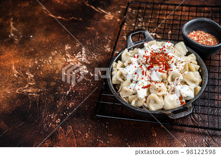 Cooking Manti Dumpling with yoghurt and tomato sauce in a skillet. Dark background. Top view. Copy space Cooking Manti Dumpling with yoghurt and tomato sauce in a skillet. Dark background. Top view. Copy space 98122598
