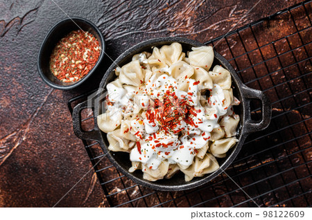 Cooking Manti Dumpling with yoghurt and tomato sauce in a skillet. Dark background. Top view Cooking Manti Dumpling with yoghurt and tomato sauce in a skillet. Dark background. Top view 98122609