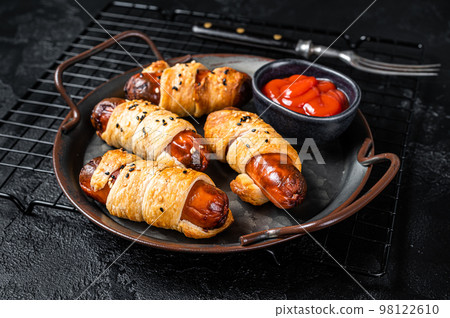 Pigs in Blanket puff pastry sausage wrap roll. Black background. Top view 98122610