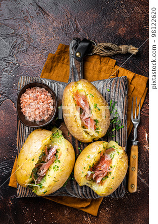 Jacket potatoes baked with cheese, herbs and butter. Dark background. Top view 98122620