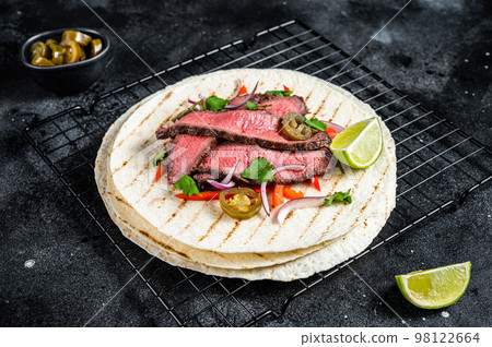 Grilled Beef steak Fajitas, taco tortillas with onion, jalapeno and bell pepper. Black background. top view Grilled Beef steak Fajitas, taco tortillas with onion, jalapeno and bell pepper. Black background. top view 98122664