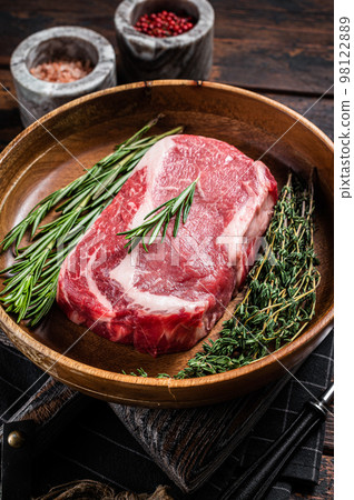 Rib-eye raw Steak, rib eye beef marbled meat in wooden plate with rosemary and thyme. Wooden background. Top view 98122889